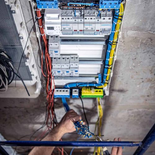 A male electrician works in a switchboard with an electrical connecting cable.
