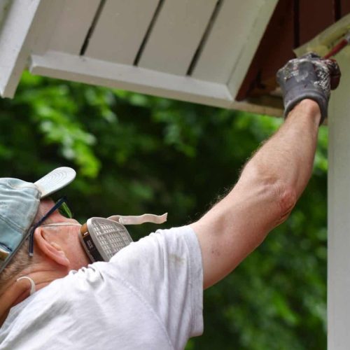 A man painting house exterior with white color