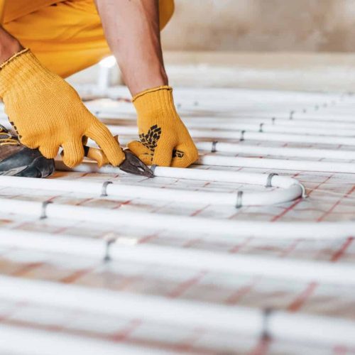 Close up view. Worker in yellow colored uniform installing underfloor heating system