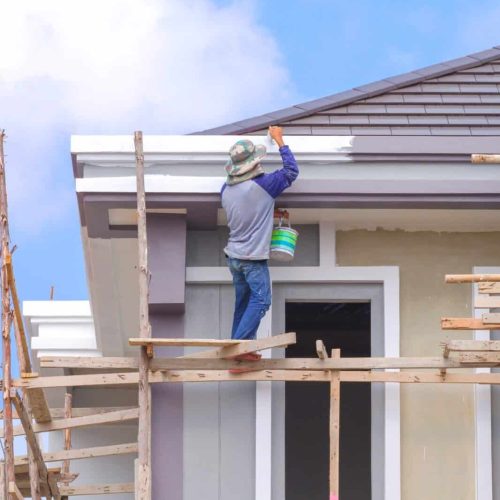 Painter on wooden scaffolding is painting roof eaves of modern house structure in construction site