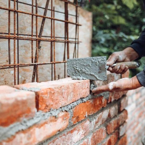 Professional worker using pan knife for building brick walls with cement and mortar